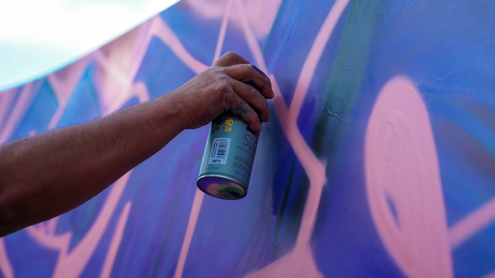 Artist spraying pink over a blue mural. Photo by Cesareo Sifuentes